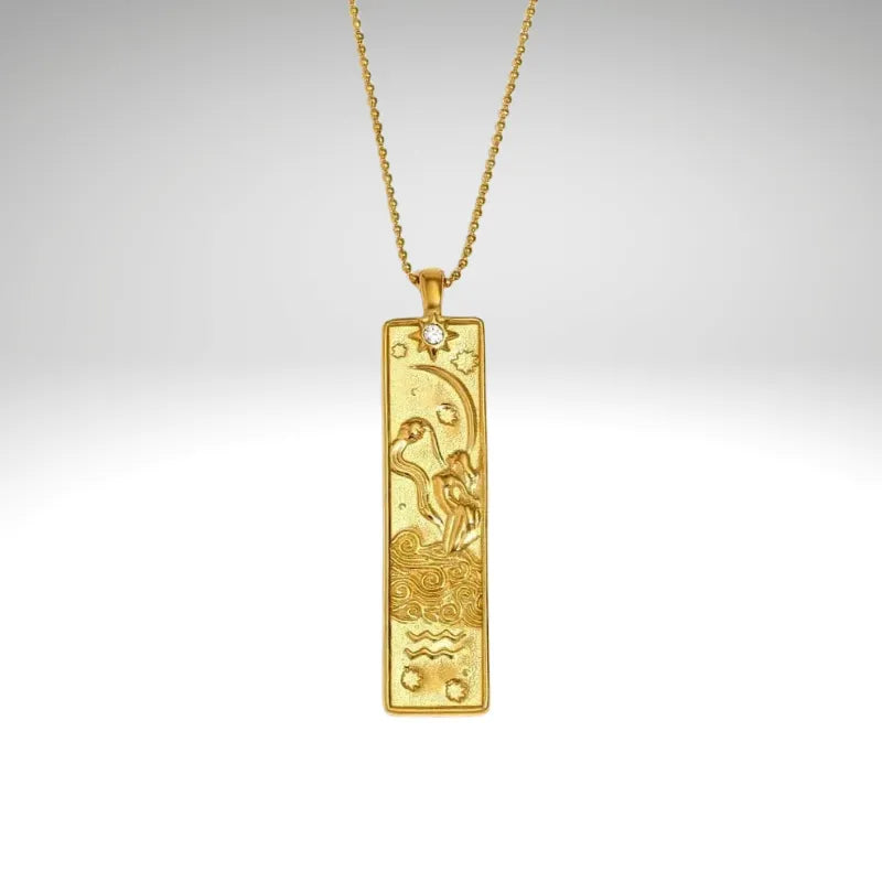 Gold pendant with zodiac design on a chain against a light gray background