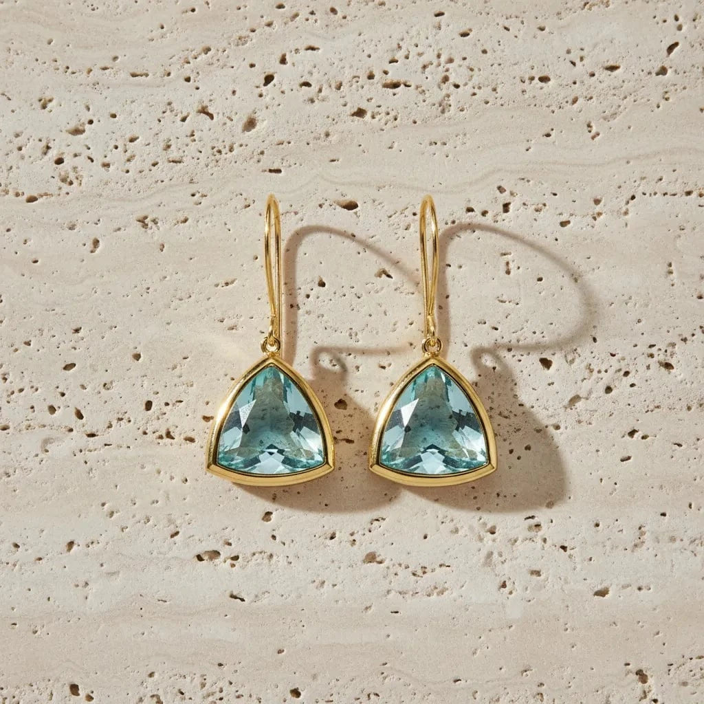 Gold earrings with blue gemstones on a beige stone surface