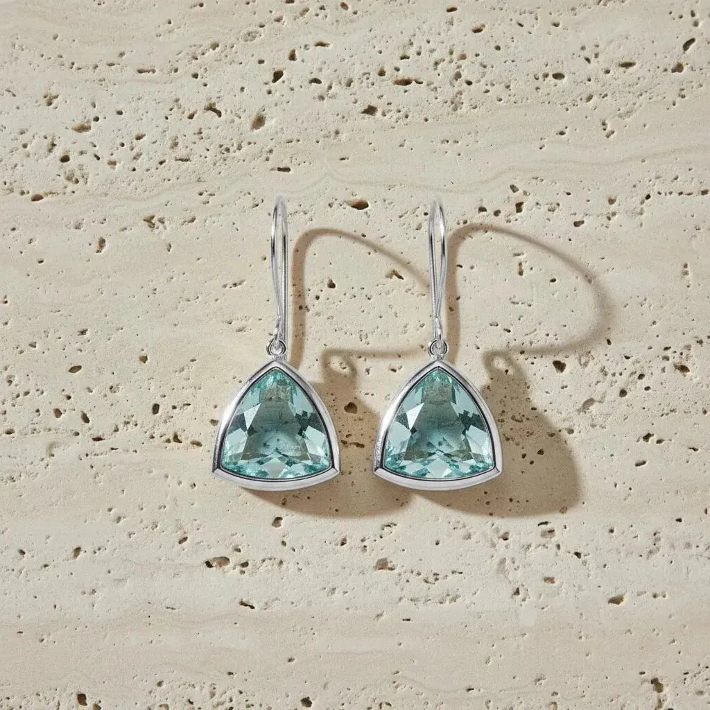 Teardrop-shaped turquoise earrings on a beige stone background