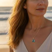 Woman on beach wearing aqua Aria teardrop pendant necklace in gold, March birthstone jewelry