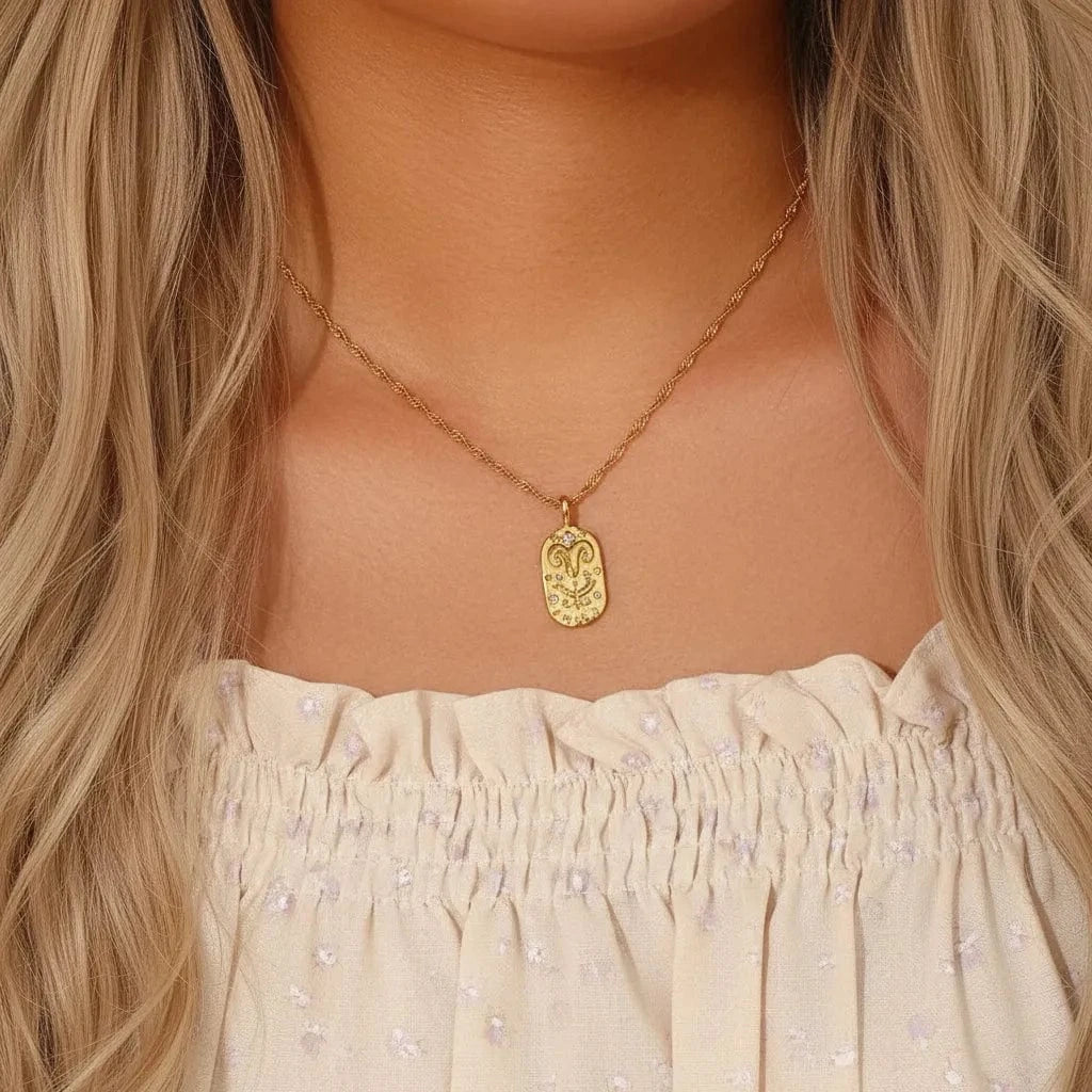 Gold necklace with a pendant worn by a person with purple hair, wearing a floral top.
