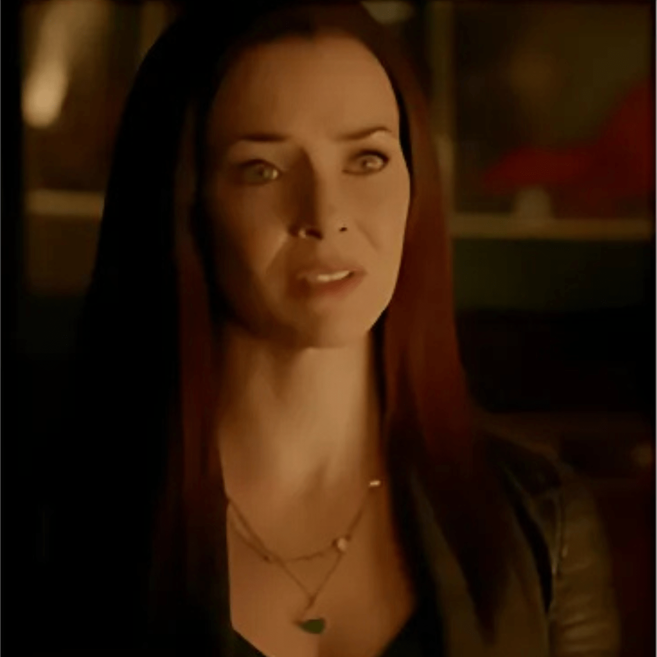 Woman with long hair wearing layered necklaces in a dimly lit setting