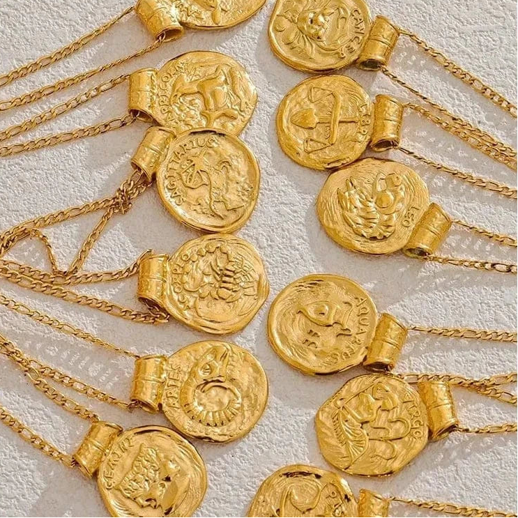 Gold necklaces with coin pendants on a textured white background