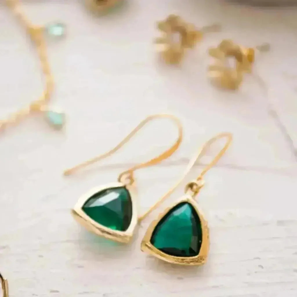 Gold earrings with green gemstones on a light background