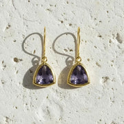 Pair of gold earrings with purple gemstones on a textured beige surface