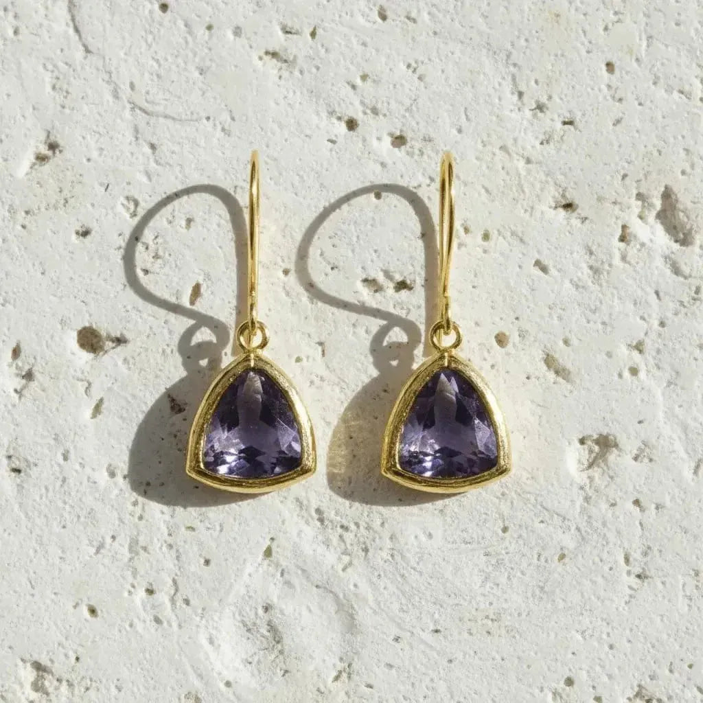 Pair of gold earrings with purple gemstones on a textured beige surface