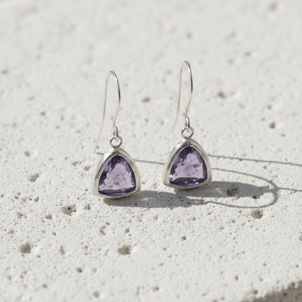 Pair of silver earrings with purple gemstones on a textured white surface
