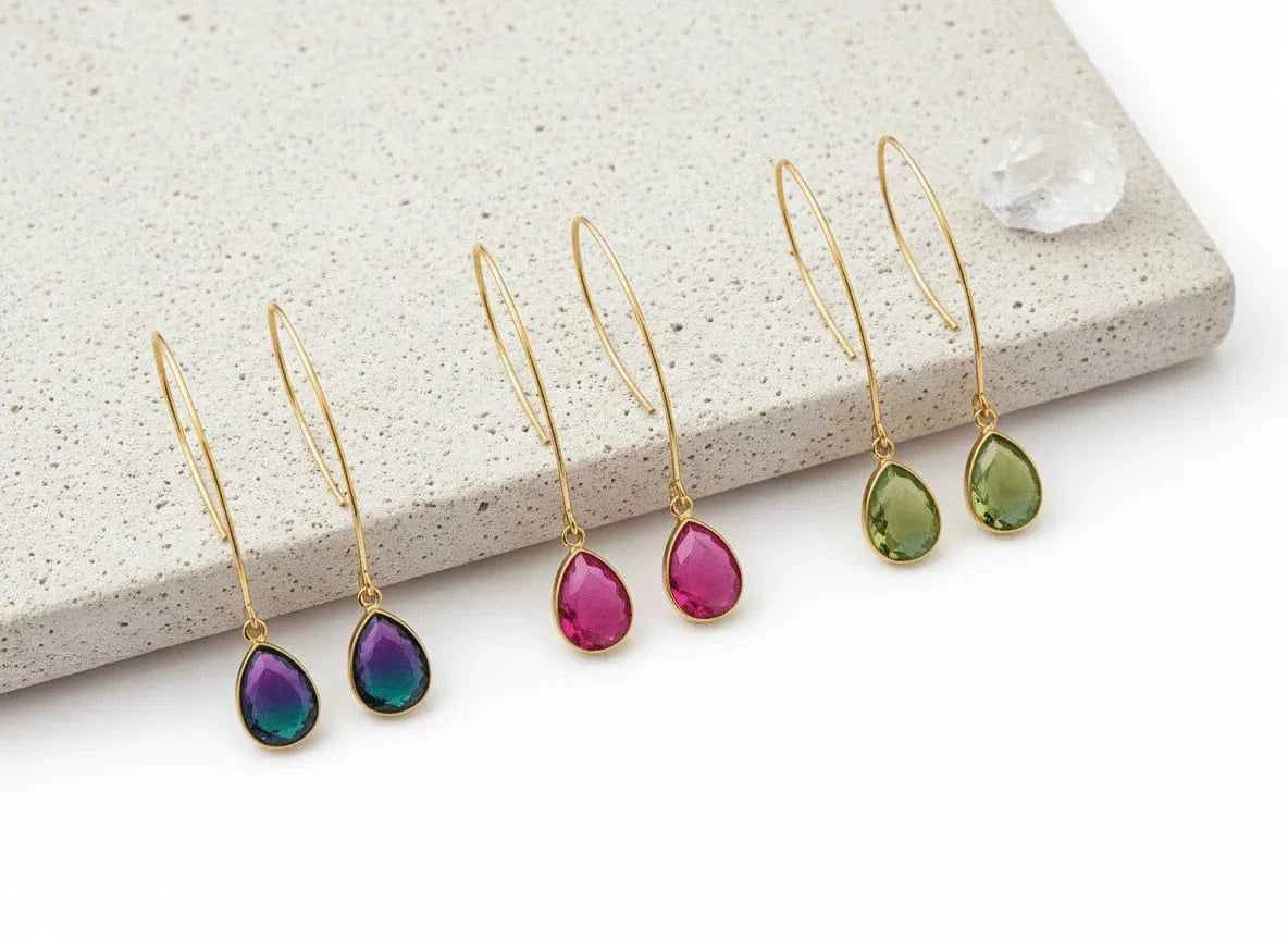 Set of gold earrings with colorful teardrop stones on a stone surface