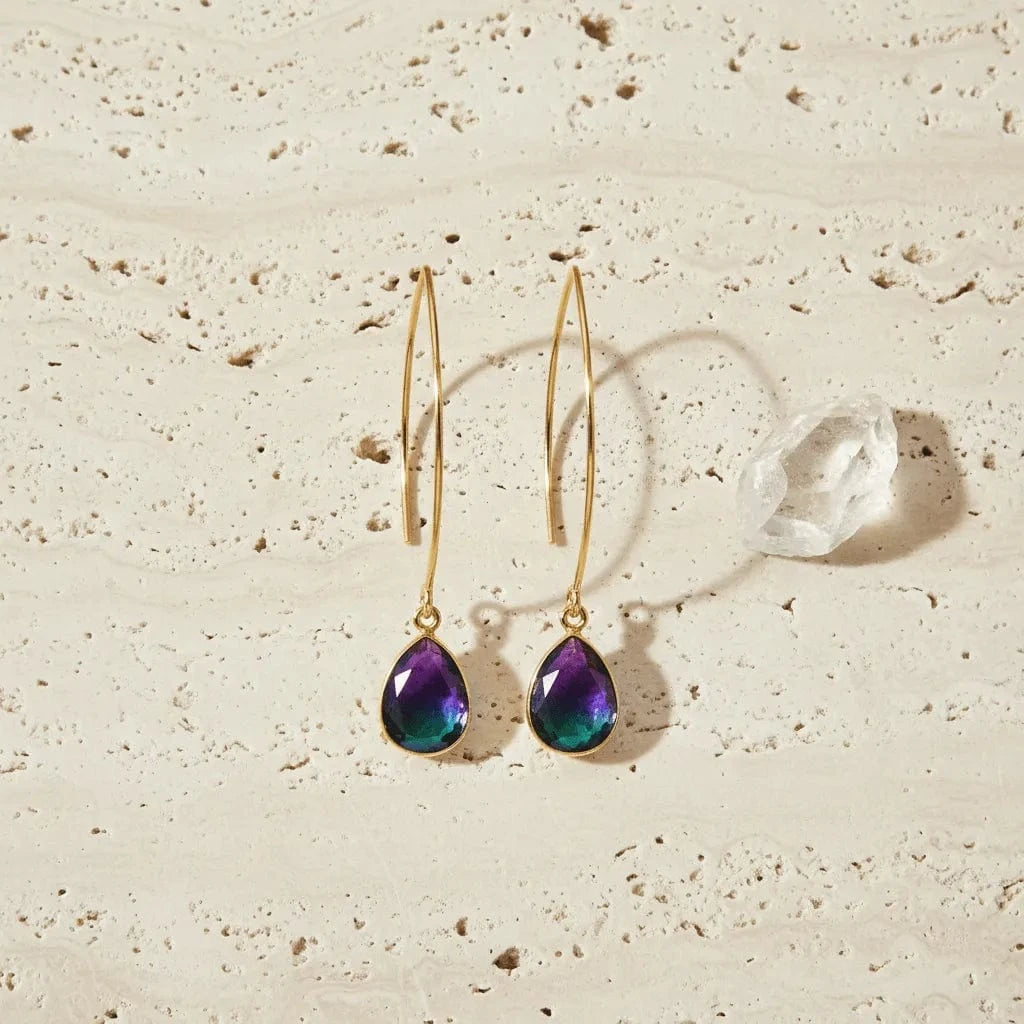 Gold earrings with purple teardrop stones on a beige surface