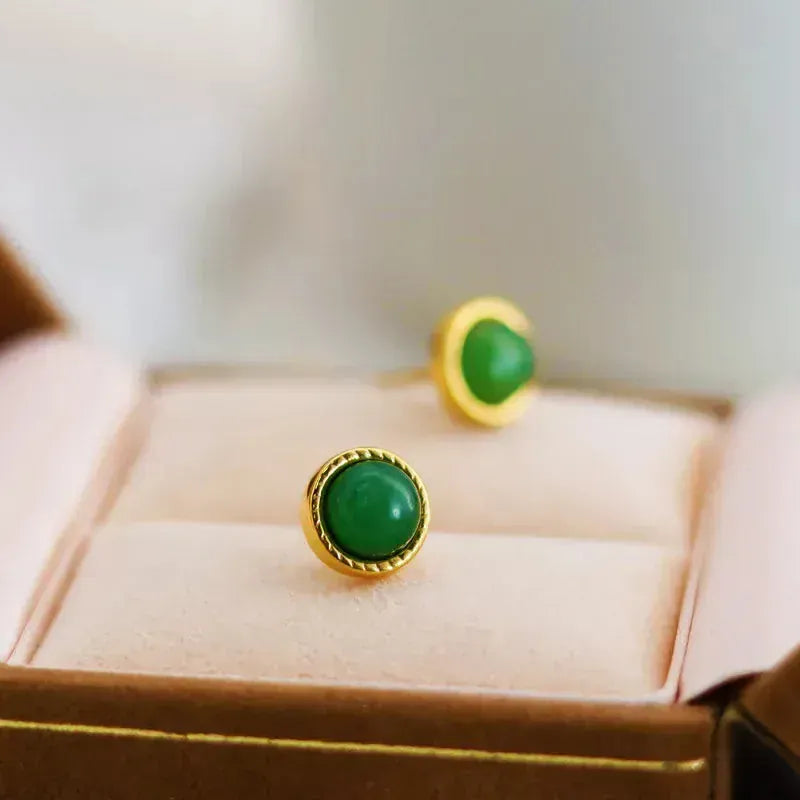 Green gemstone earrings with gold settings on a pink jewelry box.