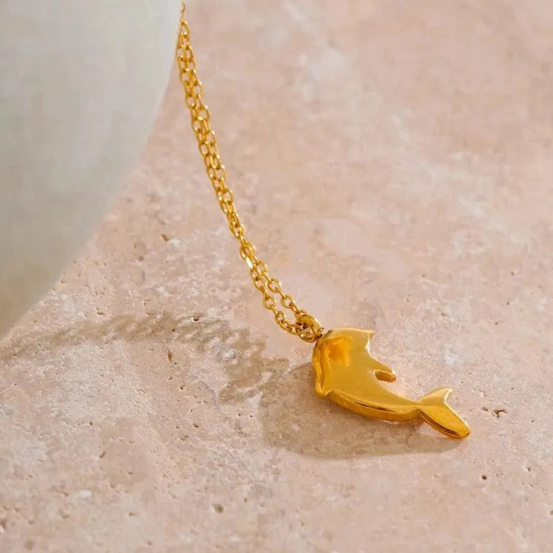 Gold dolphin pendant necklace on a textured beige surface with 'SCENE DRAWING' text above.