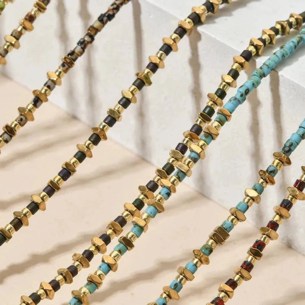 Multiple beaded necklaces with gold, black, and turquoise beads on a neutral background