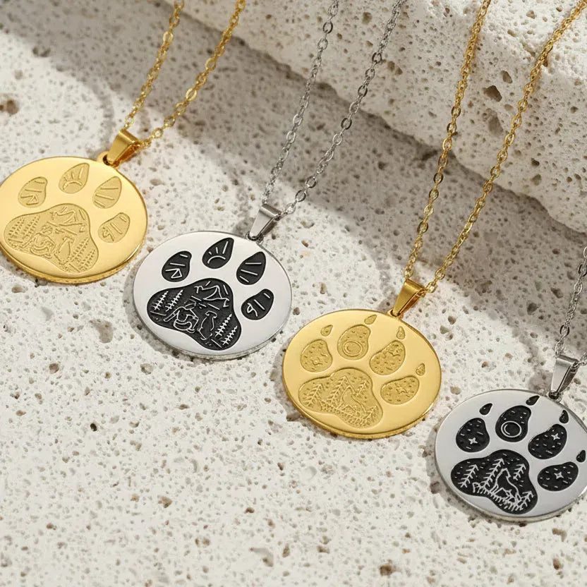 Four paw print necklaces in gold and silver on a pink background