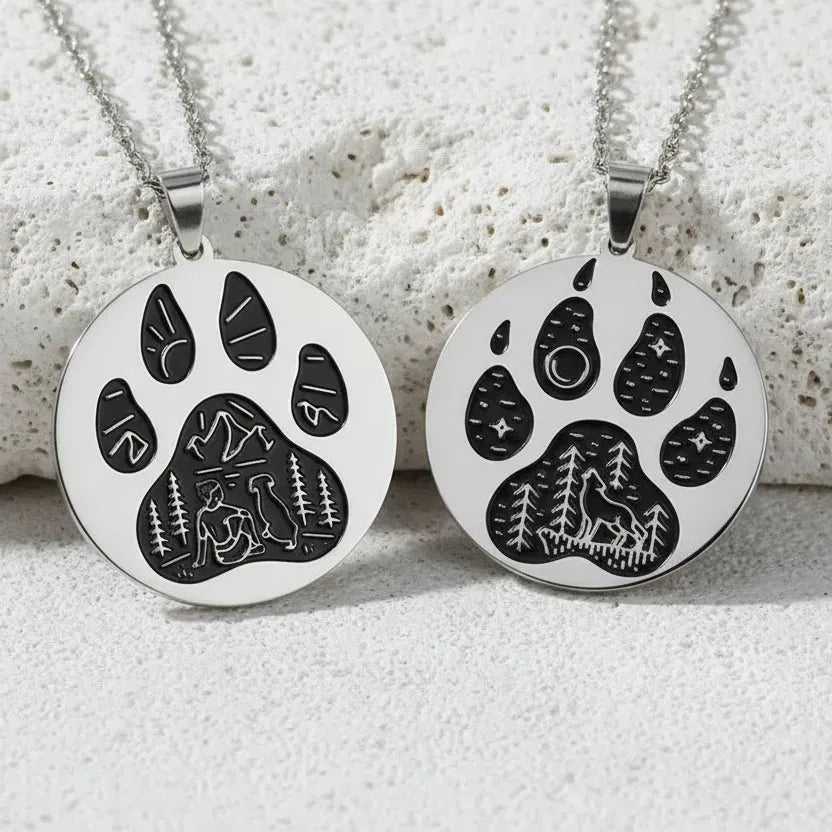 Two silver paw print necklaces on a light pink background