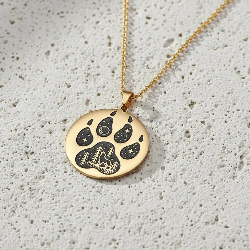 Gold necklace with a paw print pendant on a white surface