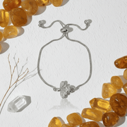 Gold bracelet with a butterfly charm on a white background with pink stones and branches.