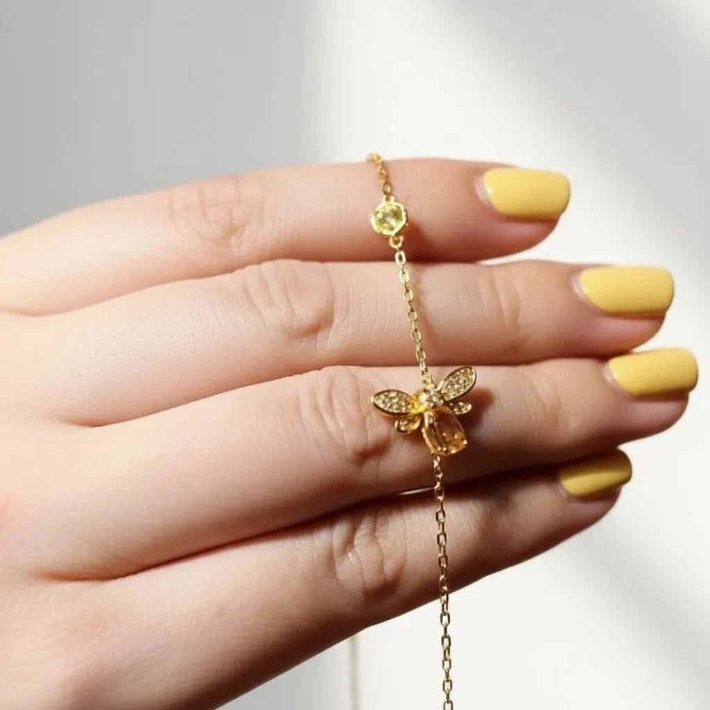 Close-up of a woman's hand with gold jewelry, including a ring and bracelet, against a blurred background.