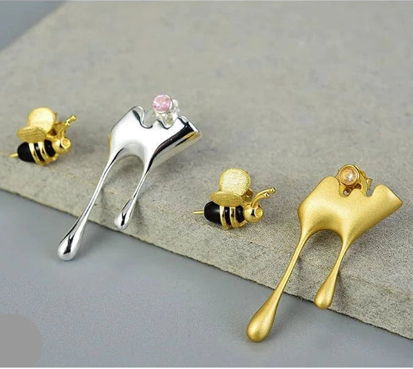 Gold, silver, and bronze bee-shaped earrings on a gray surface.