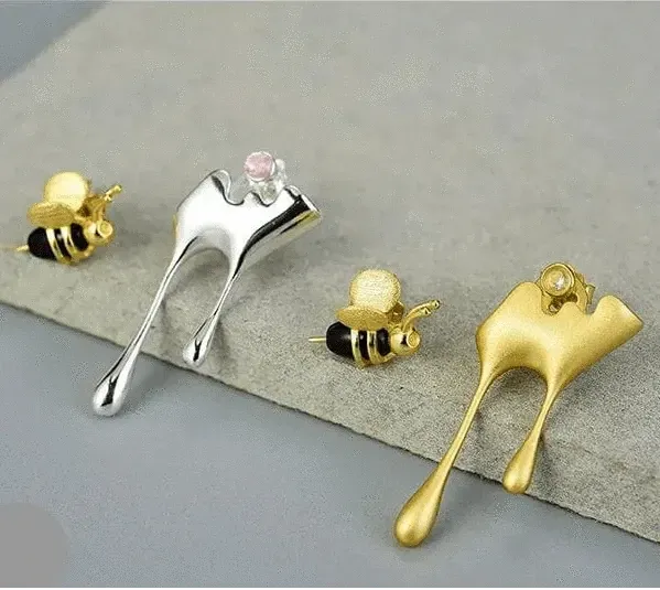 Gold, silver, and bronze bee-shaped earrings on a gray surface.