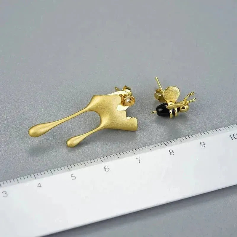 Gold bee-shaped earrings on a gray surface with a ruler for scale.