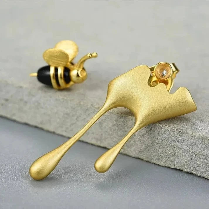 Gold bee and leaf-shaped earrings on a gray surface