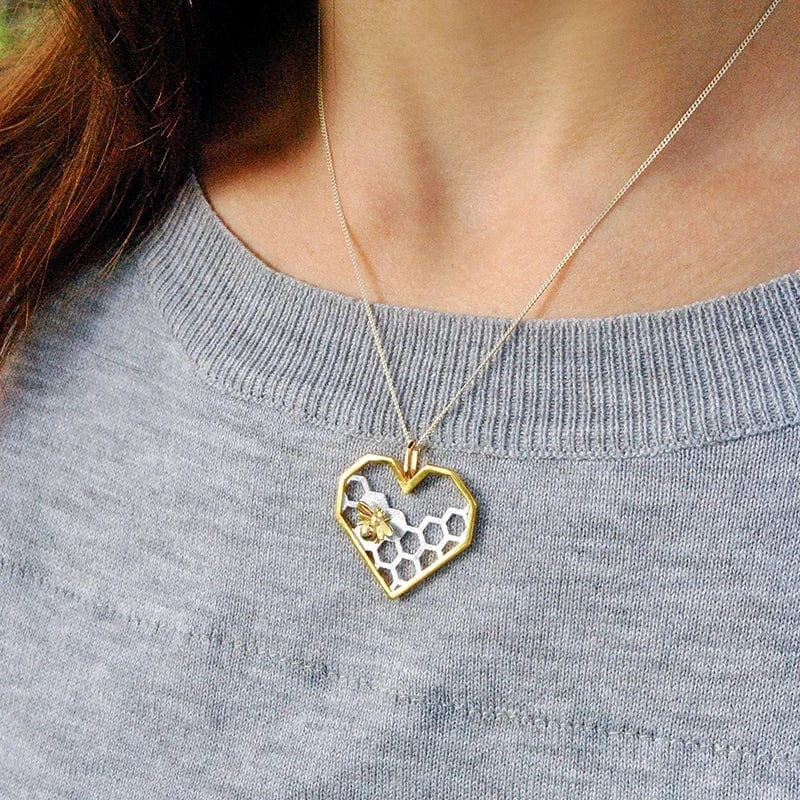 Heart-shaped necklace with a honeycomb design worn by a person in a gray sweater.