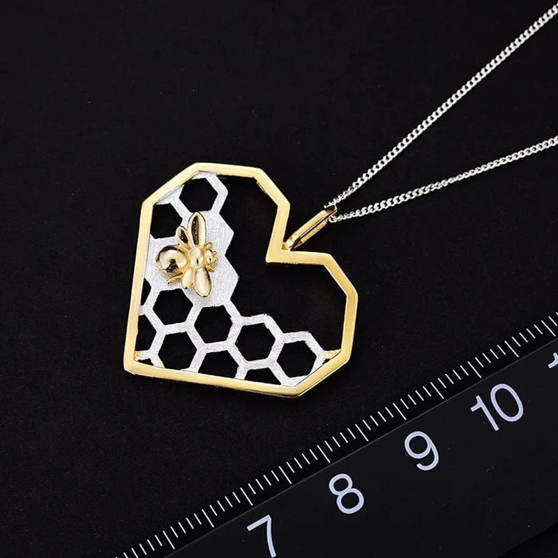 Necklace with a heart-shaped pendant featuring a honeycomb design and bee on a black background with a ruler for scale.