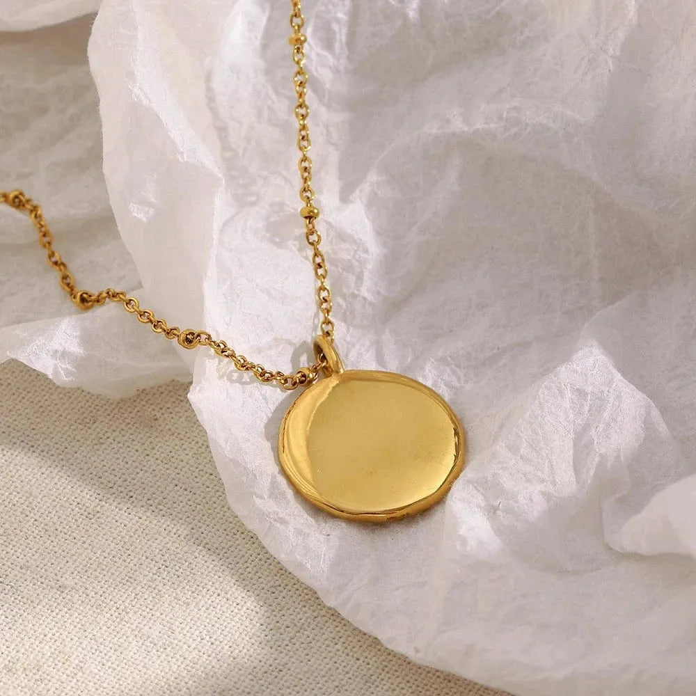 Gold necklace with a round pendant on a textured white surface