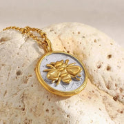 Gold and silver bee pendant necklace on a textured stone surface
