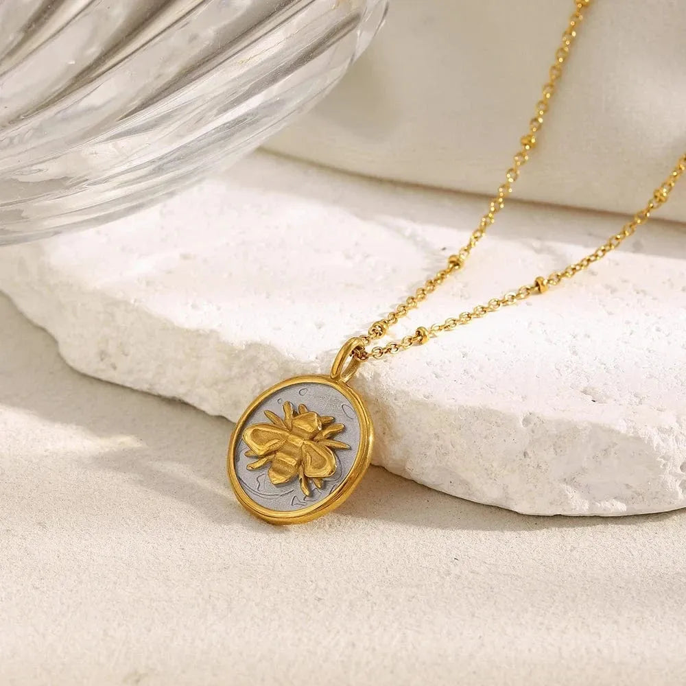 Gold necklace with a round pendant featuring a bee design on a light stone surface.