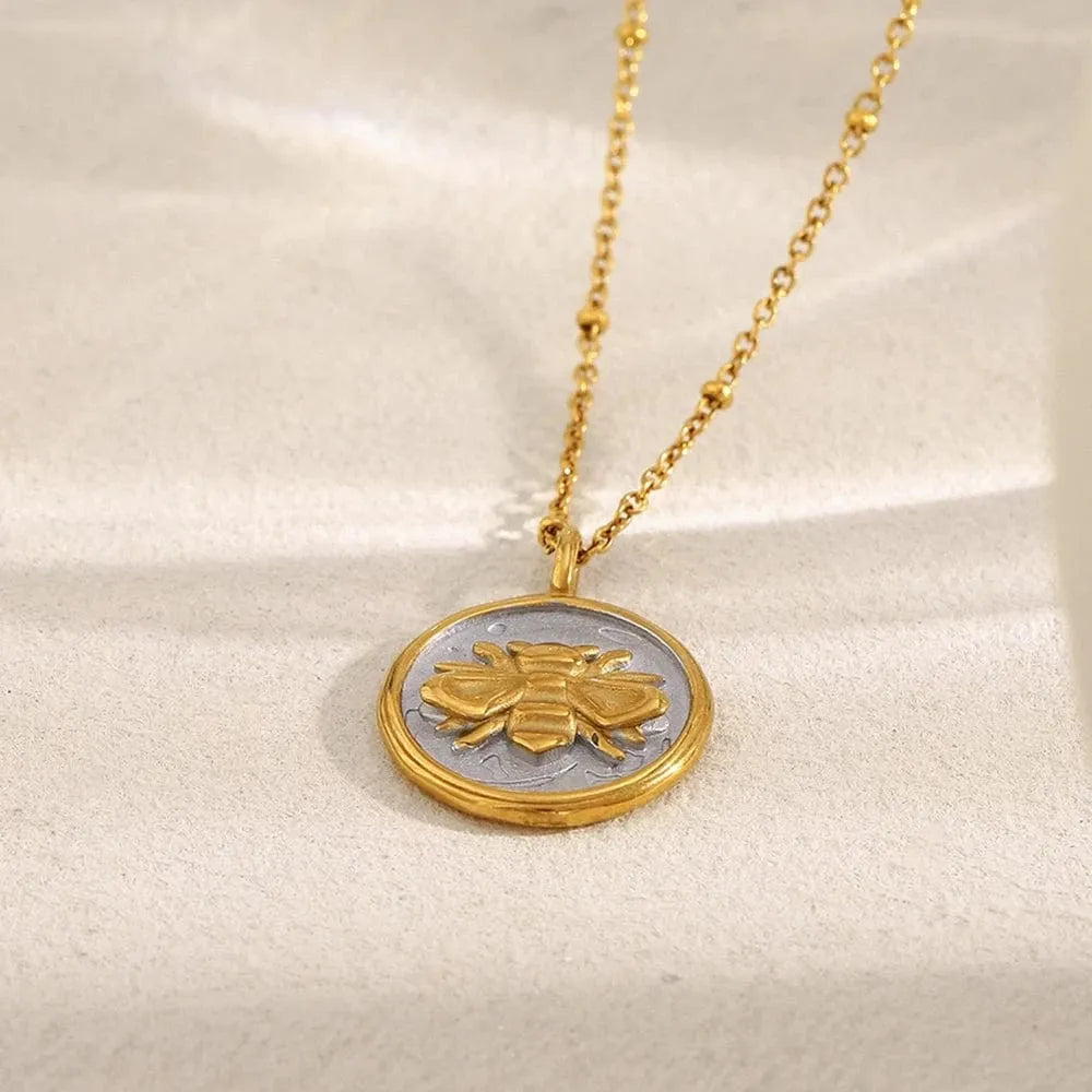 Gold necklace with a round pendant featuring a bee design on a beige background