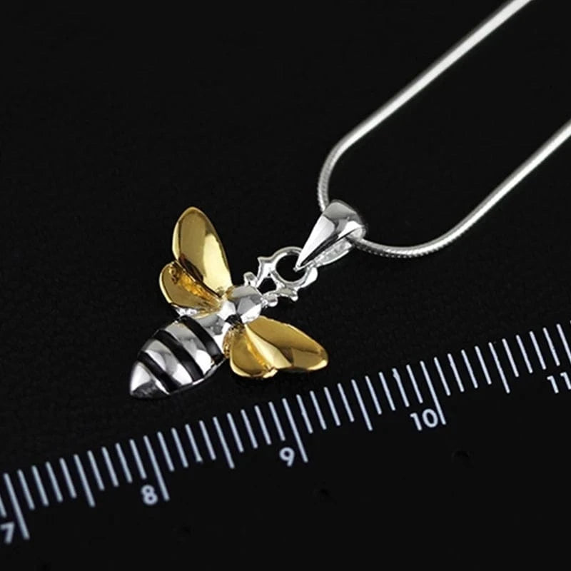 Gold and silver bee-shaped pendant on a black background with a ruler for scale.