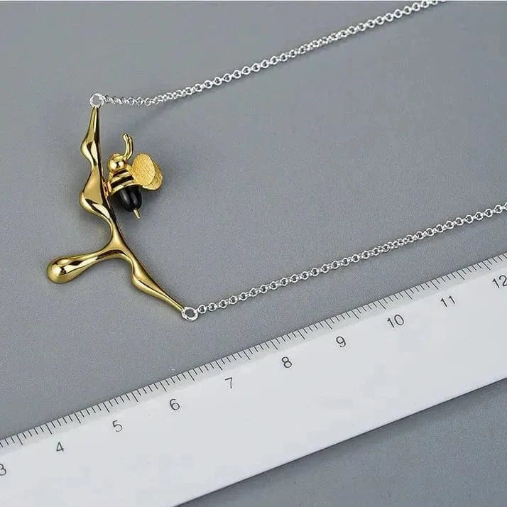 Gold and silver necklace with a unique pendant on a gray surface next to a ruler.