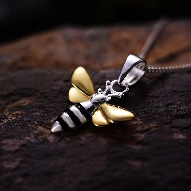 Gold and silver bee-shaped pendant on a dark surface