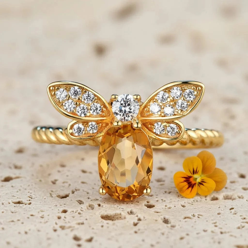 Gold bee-shaped ring with a large orange gemstone on a light background