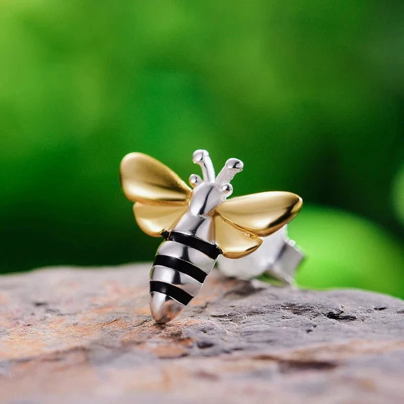 Silver and gold bee-shaped earring on a wooden surface with a green blurred background
