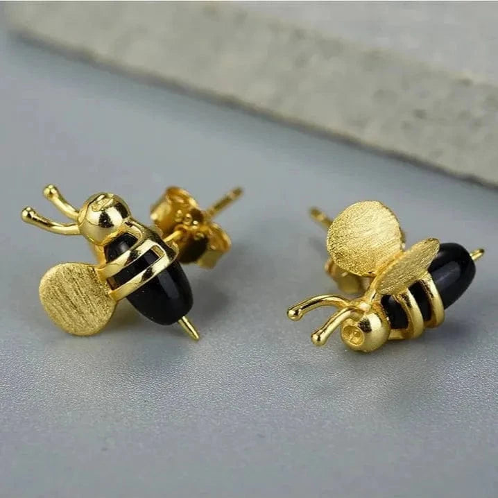 Gold bee-shaped earrings with black accents on a gray surface
