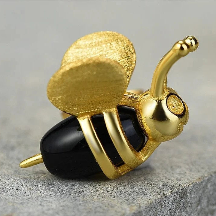 Gold and black bee-shaped object on a gray surface