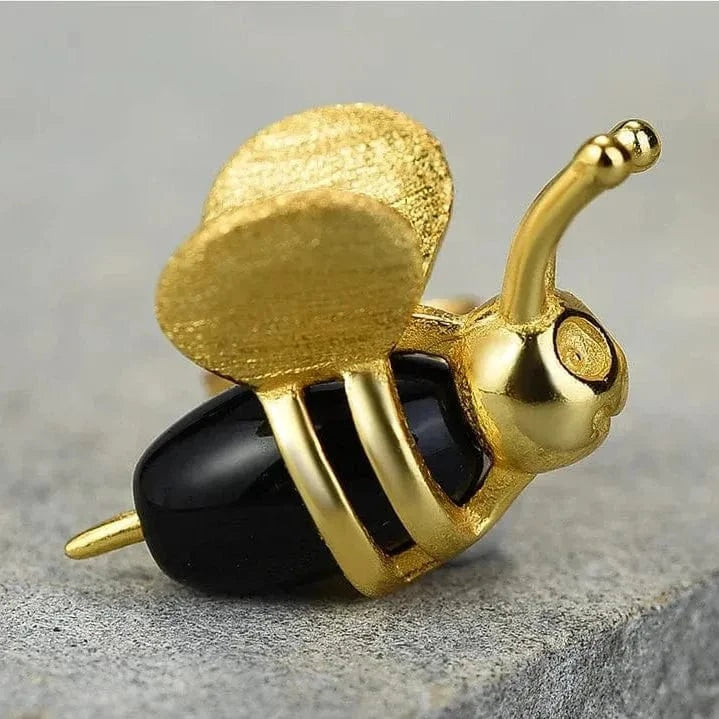 Gold and black bee-shaped object on a gray surface