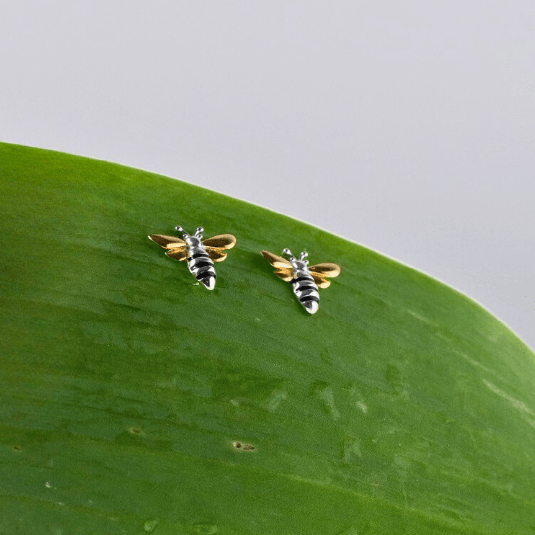 Bee-shaped earrings on a green leaf with a light gray background