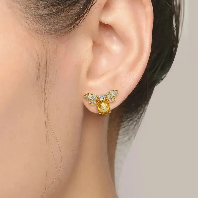 Gold bee-shaped earring worn on an ear with a neutral background