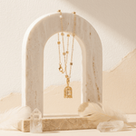 Gold necklace with a birdcage pendant on a marble arch