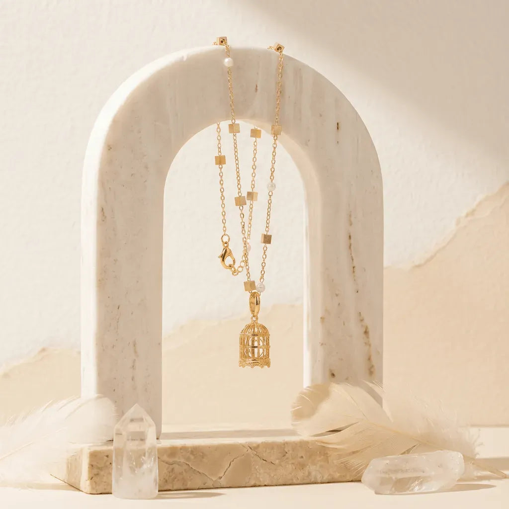 Gold necklace with a birdcage pendant on a marble arch