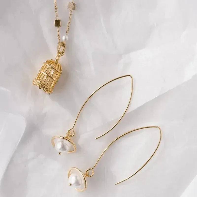 Gold earrings with pearl-like beads on a white fabric background