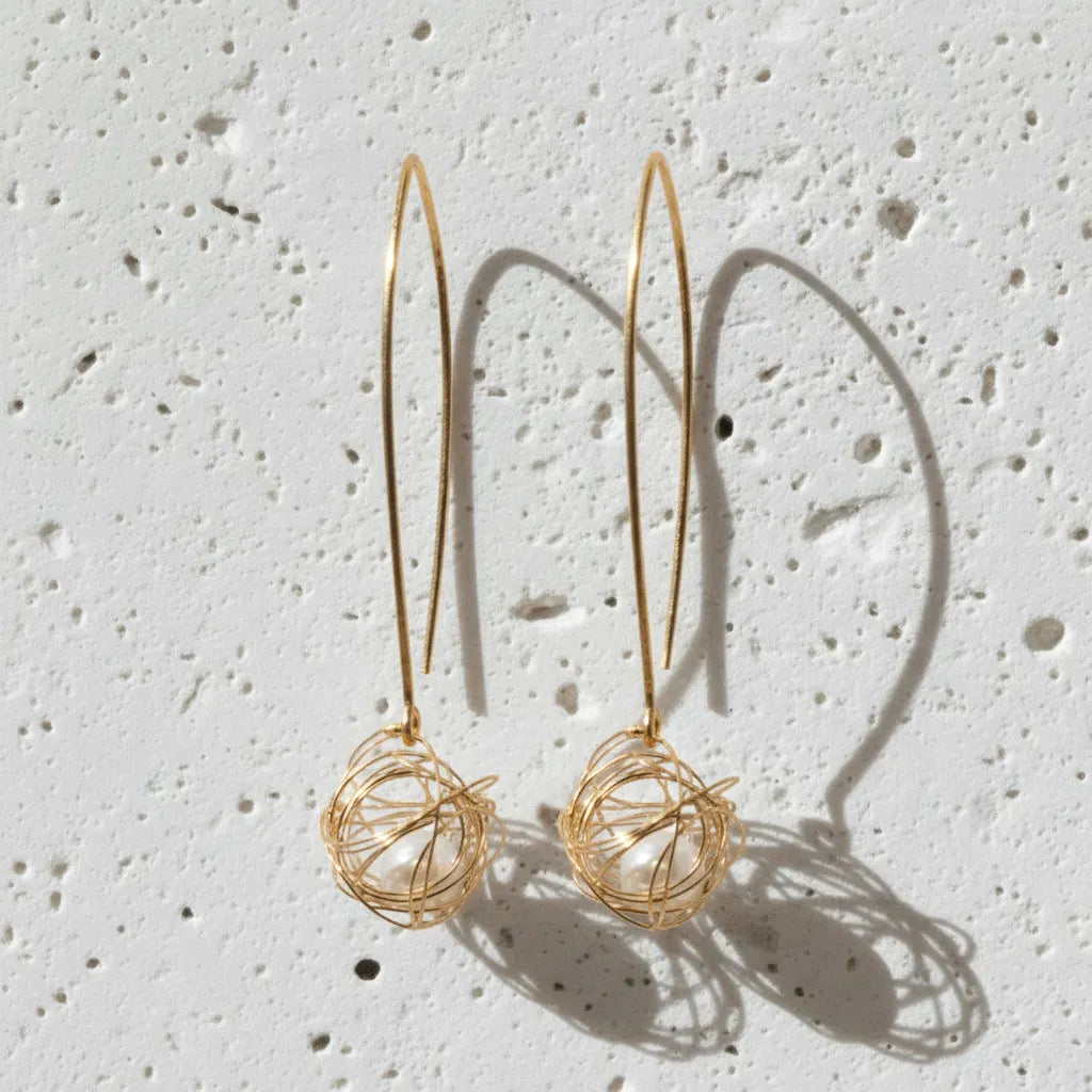 Gold wire basket earrings on a textured white surface