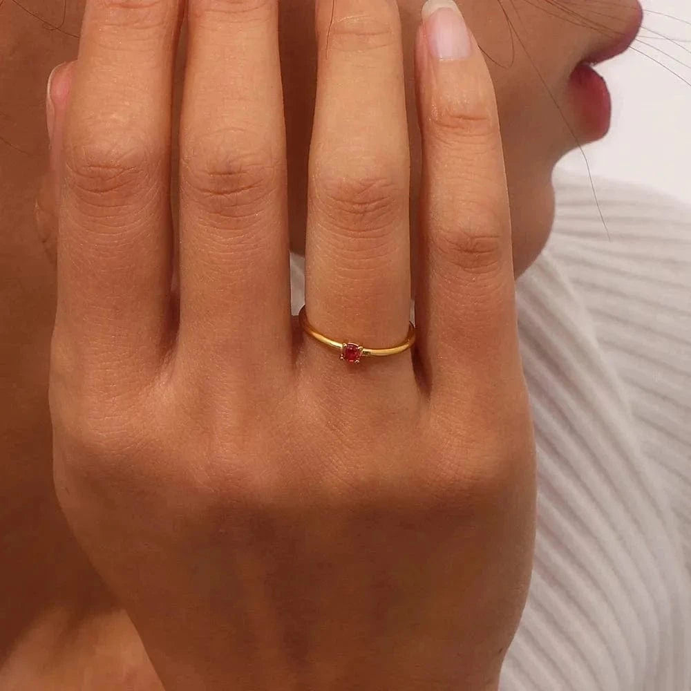 Close-up of a hand wearing a gold ring with a red gemstone.