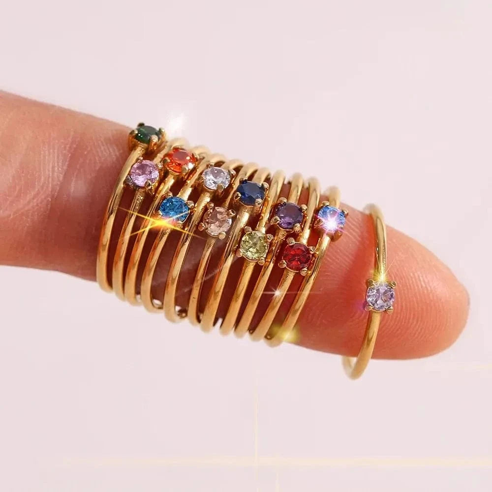 Gold ring with colorful gemstones on a finger against a light background