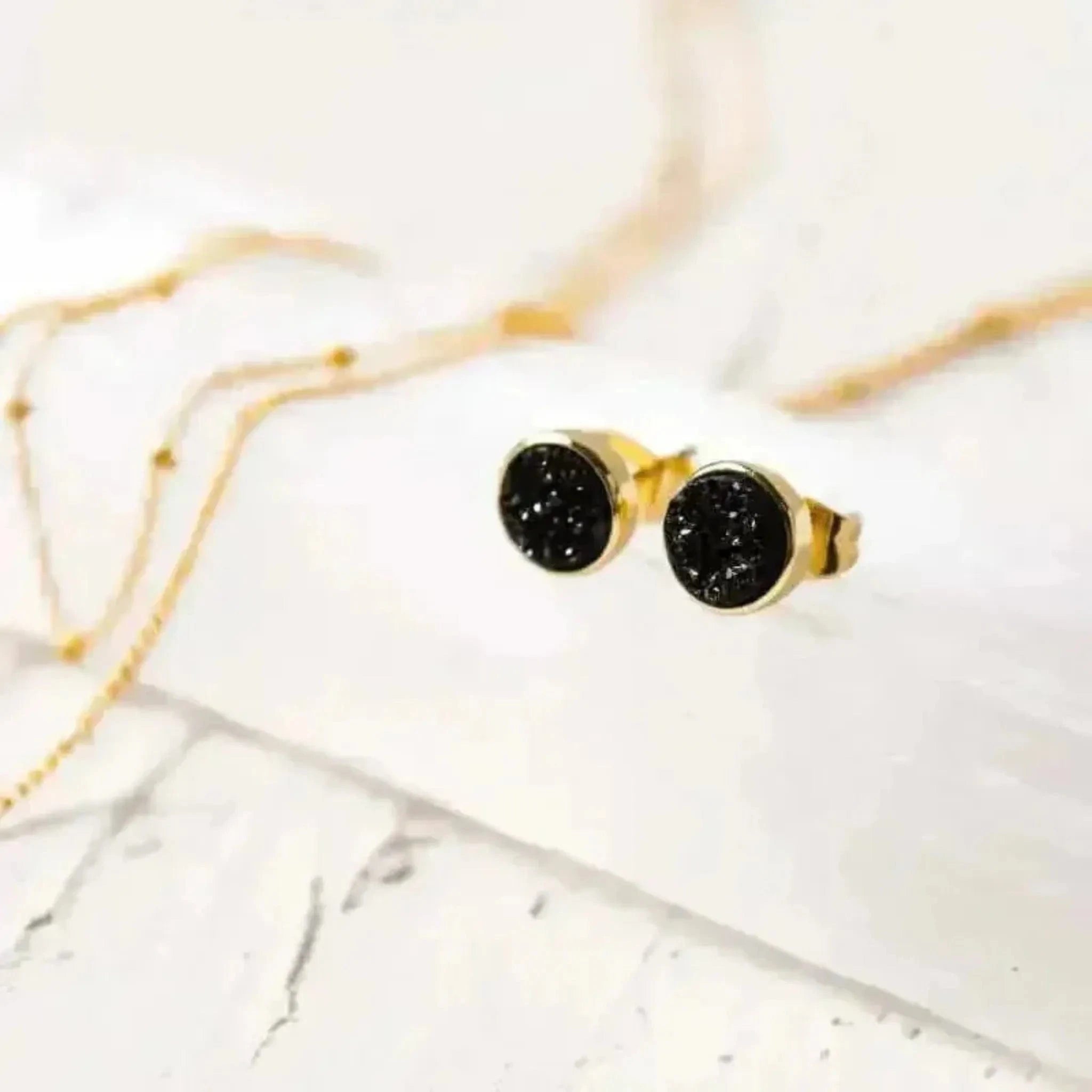 black druzy agate round stud earrings in gold on a selenite crystal