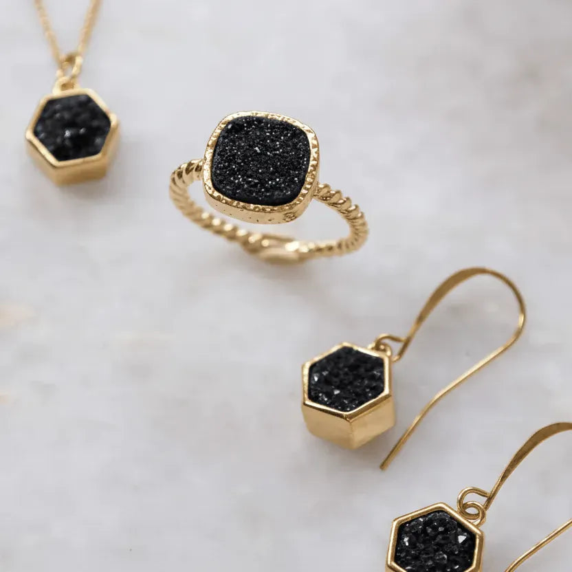 Gold jewelry set with black gemstones on a marble surface