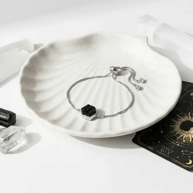 Silver bracelet with a black gemstone on a white dish, surrounded by tarot cards and crystals.